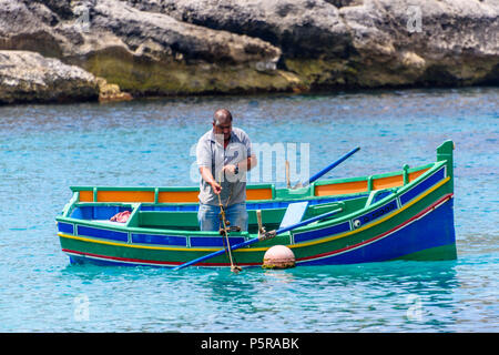 Un pescatore di righe il suo tradizionale maltese barca a remi nella baia di Xlendi a raccogliere le gabbie di aragosta. Foto Stock