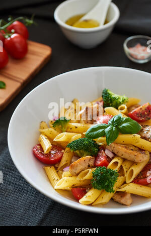 Il cibo italiano. Fusilli insalata di pasta con condimento italiano, pomodori, broccoli e le foglie di basilico sul tessuto nero lo sfondo. Pasto delizioso. Foto Stock