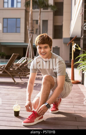 Giovani asiatici legatura a runner i suoi lacci delle scarpe all'esterno. Foto Stock