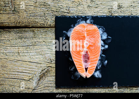 Filetti di Salmone su ghiaccio su tavoli in legno nero vista dall'alto. Alimenti per pesci concetto. Copia dello spazio. Foto Stock