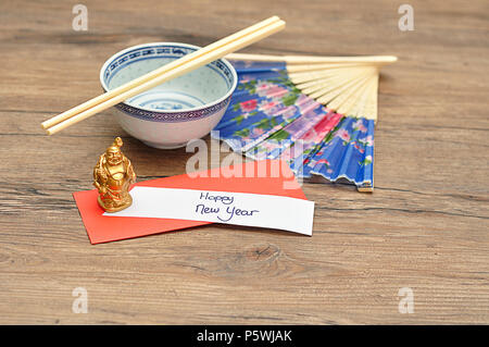 Anno Nuovo Cinese design. Una busta rossa del denaro per il Nuovo Anno Cinese e una nota di felice anno nuovo con una ciotola, bastoncini, lato ventola e un Buddha fi Foto Stock