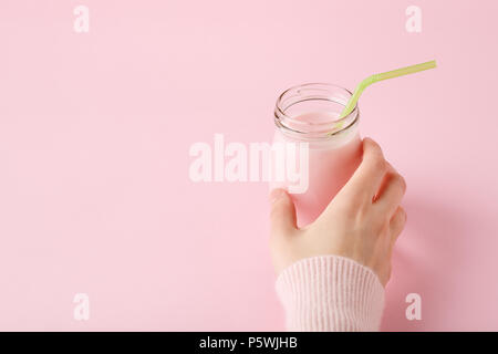 Le donne la mano che regge una bottiglia di vetro di yogurt alla frutta con paglia sul rosa pastello con sfondo spazio copia. Bibita salutare concetto, minima. Foto Stock