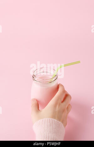 Le donne la mano di prendere una bottiglia di vetro di yogurt alla frutta con la paglia. Rosa pastello con sfondo spazio copia. Uno stile di vita sano concetto, minimale, verticale. Foto Stock