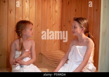 Due ragazze hanno essi stessi avvolti in asciugamani e sono seduti in una sauna finlandese Foto Stock