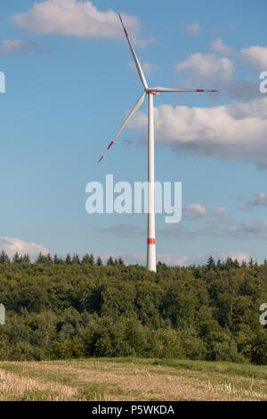 Una turbina eolica sorge nella foresta e genera elettricità verde attraverso la produzione sostenibile di energia elettrica Foto Stock