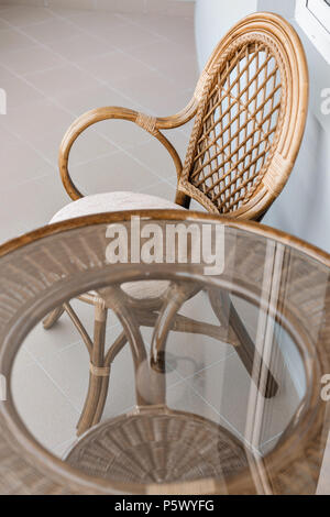 Tavolo in vetro e rattan vimini sedia sedile. Arredamento in vimini rattan tabella due sedie vicino alla finestra sul balcone Foto Stock