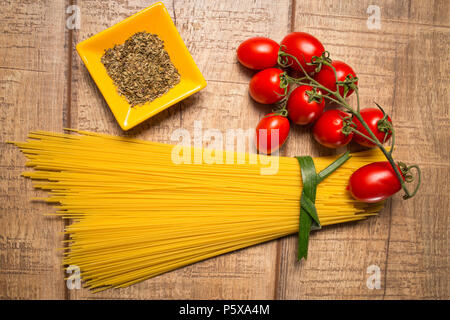 Gli spaghetti e Roma i pomodori isolate su tavola di legno dello sfondo. Non cotti italiano spaghetti secchi. Vista dall'alto. Lay piatto. Foto Stock