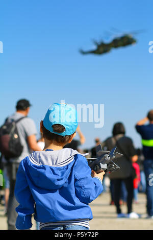 Timisoara, Romania - Giovane ragazzo con aeroplano giocattolo in mano ammirando il Romanian Air Force IAR 330 elicotteri Puma di eseguire una dimostrazione di volo Foto Stock