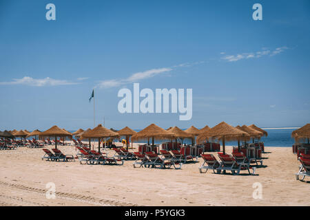 Giugno 21st, 2018 Bico das Lulas Beach, Troia, Portogallo - ombrelloni di paglia e sedie ad una spiaggia di sabbia Foto Stock