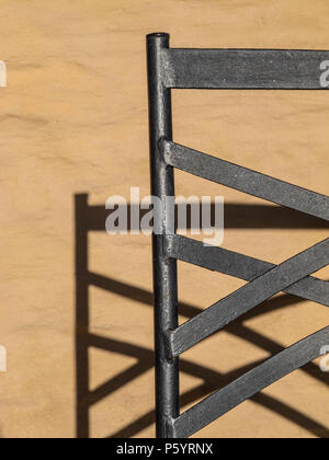 Sedia di ferro sporgente la sua ombra contro la parete dietro di essa Foto Stock