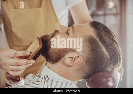 Il barbiere pettini l'uomo con la barba con un pennello. Foto in stile vintage Foto Stock