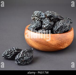 Le prugne secche nella ciotola di legno con gocce d'acqua su sfondo nero Foto Stock