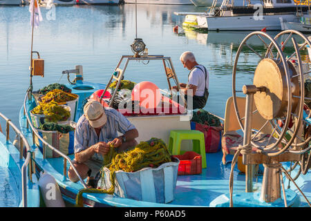 I pescatori locali riassettavano le reti da pesca su un tradizionale locale in stile barca da pesca nel vecchio porto di Ayia Napa, Cipro Foto Stock