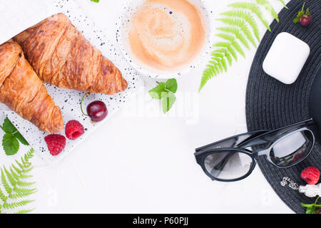 Donna accessori, lady in vacanza. Occhiali da sole e cappello, croissant e caffè per colazione. Sfondo bianco. Copia dello spazio. Lay piatto. Foto Stock