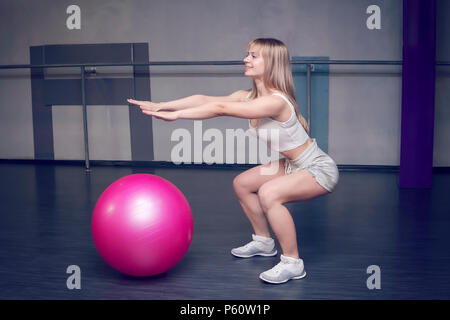 Montare la giovane donna graziosa facendo esercizi SQUAT CON PALLA fitness. vista laterale Foto Stock