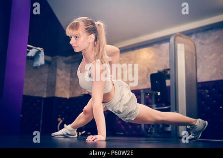 Foto del profilo di un preciso e potente forte bella enduring donna con capelli biondi e coda di cavallo taglio di capelli in piedi sulle mani facendo plank e spingere Foto Stock