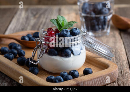 Cheesecake parfaits color crema con mirtilli e ribes rosso bacche servita nella jar, deliziosa estate no-bake dessert su tavola in legno rustico pronto a mangiare Foto Stock