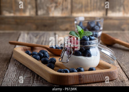 Cheesecake parfaits color crema con mirtilli e ribes rosso bacche servita nella jar, deliziosa estate no-bake dessert su tavola in legno rustico pronto a mangiare Foto Stock