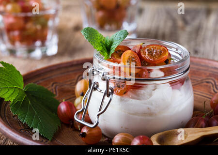 Cheesecake parfaits color crema con uva spina nella jar, deliziosa estate no-bake dessert su tavola in legno rustico pronto a mangiare Foto Stock