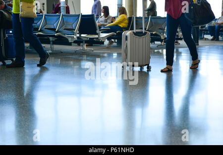 Una vista di persone, alcuni seduti mentre altri stanno facendo la loro strada attraverso il terminal di un aeroporto con pavimenti riflettente,rullo operativo bagagli in avanti e indietro Foto Stock