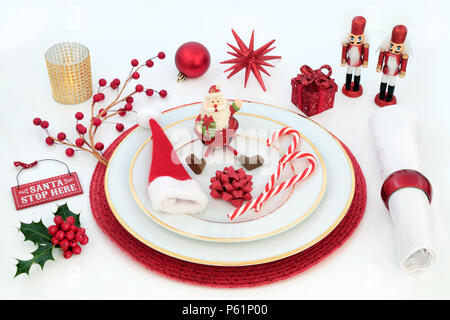 Cena di Natale divertente messa in tavola con piatti di porcellana, ninnolo decorazioni, igienico, candela e l'inverno holly su sfondo bianco. In tema natalizio conc Foto Stock