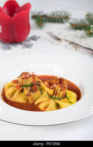 Fagottini al forno di pasta ripiena di ricotta e serrati con erba cipollina fresca, su salsa di pomodoro, piatto tipico della cucina italiana. Foto Stock