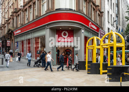 I pedoni a piedi al di fuori del negozio Vodaphone in Corporation St, centro della città di Birmingham, UK. Anti-terrorismo ostacoli sulla giunzione nella nuova strada. Foto Stock