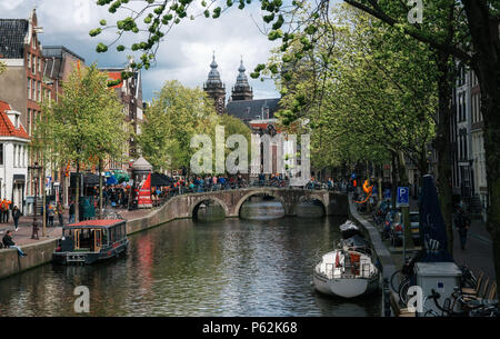 Amsterdam, Paesi Bassi - 25 April, 2017: Houseboats e chiatte viventi contro il ponte. Quartiere a luci rosse de Wallen, Vista della Basilica di San Nicola Foto Stock