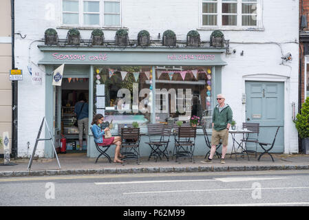 Donna seduta al tavolo della pavimentazione e uomo in piedi al di fuori delle stagioni Deli Cafe in Piazza del Mercato, Amersham Città Vecchia,Buckinghamshire, Inghilterra, Regno Unito Foto Stock