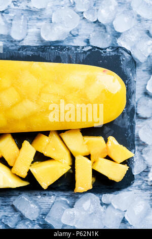 Alta anble colpo di ghiaccio in casa pop realizzata con ananas naturale o di mango, su un naturale vassoio ardesia circondato da ghiaccio Foto Stock