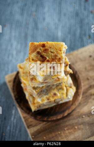 Alcuni pezzi di tipico la tortilla de patatas, frittata spagnola, su una lastra di legno, collocata sul grigio di una tavola in legno rustico Foto Stock