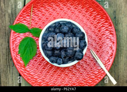 Cibo sano,l'agricoltura,raccolto e concetto di frutta: close-up di mirtilli maturi in una ciotola su una rossa piastra ceramica. Foto Stock