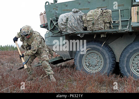 Il personale Sgt. Jorge Ramirez, un fuoco indiretto fantassin assegnato alla sede centrale e sede di truppe, 3° Stormo, 2° reggimento di cavalleria, segna un'area intorno alla sua Stryker combattimento corazzati veicolo utilizzando un piccone, che permetterà ai tecnici di scavare la dimensione corretta posizione di combattimento, 5 Aprile a Adazi Base Militare, Lettonia. Soldati utilizzato un D6 bulldozer e una elevata mobilità engineer escavatore per scavare le posizioni di combattimento per strykers e alleati lettone prima di una multinazionale di difesa combinata live-fire esercizio a sostegno del funzionamento Atlantic risolvere, una multinazionale di dimostrazione ha continuato U.S. Foto Stock