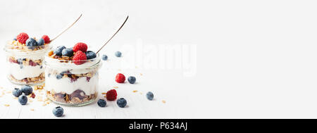 Due vasi con gustosi parfaits fatta di granola, bacche e yogurt bianco su un tavolo di legno. Girato ad angolo con posto per testo, banner. Foto Stock