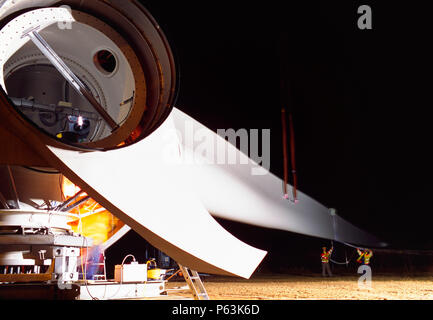 Lunga immagine di esposizione dei lavoratori il montaggio del mozzo e delle pale di un gigante Enercon turbina eolica durante la notte. Foto Stock