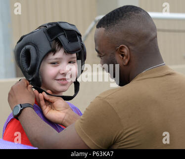 Stati Uniti Navy Petty Officer 1. Classe Aaron Gaskins, fissa acconciature per un bambino durante il giunto Senior leader arruolato campo divertente evento della durata di un giorno presso il Camp Lemonnier, Gibuti, Aprile 29, 2016. Durante l'evento, le famiglie degli STATI UNITI Ambasciata ha partecipato a un bastone pugil concorrenza, sacco di razza e di più, dimostrando una fitta comunità tra l'Ambasciata e i loro militari statunitensi di partner. (U.S. Air Force foto di Senior Airman Benjamin Raughton/rilasciato) Foto Stock