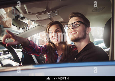 Godendo di viaggio. Bella coppia Giovane seduti sui sedili anteriori e sorridere mentre uomo bello guidare una vettura. Foto Stock