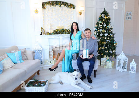 Giovane donna e uomo seduto vicino al camino e Christas tree, cane sdraiato sul pavimento. Foto Stock