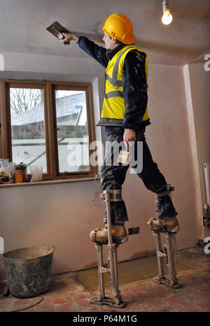 Un stuccatore su palafitte scrematura un soffitto su un cottage in ristrutturazione, REGNO UNITO Foto Stock