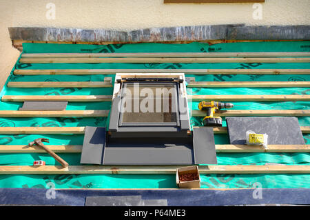 Montaggio di una finestra velux su un tetto di ardesia in costruzione che mostra la copertura traspirante feltro con bastoni di legno Foto Stock