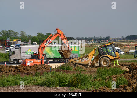 Il traffico che passa digger e macchine per movimento terra alla costruzione di strada sulla A140 Cambridge Regno Unito Foto Stock