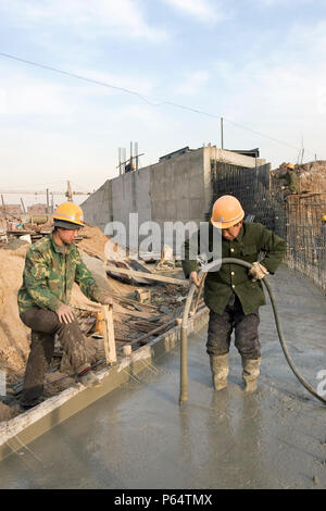 Un lavoratore utilizza un vibratore per accertarsi che non vi siano sacche di aria in una lastra di cemento che è parte di un sotto-canale di massa che andranno ad alimentare nel sud-a-n. Foto Stock