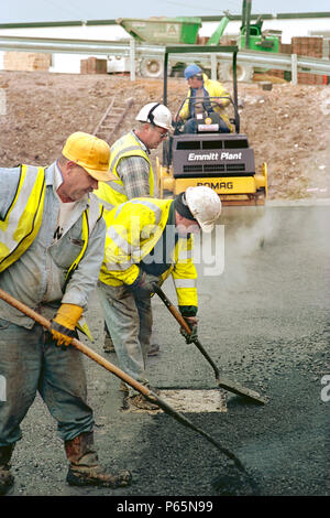 La diffusione e la laminazione chipings rivestito in laminato a caldo indossando asfalto corso utilizzando Bomag rullo vibrante. Foto Stock