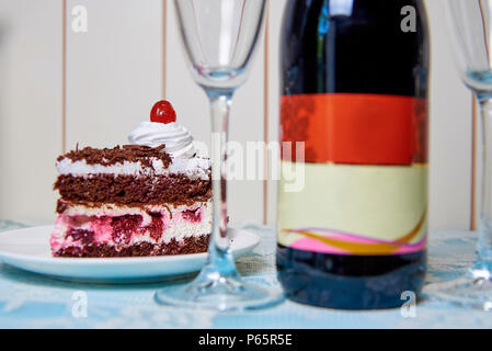 Torta al cioccolato con crema e ciliegia vicino a sfocare una bottiglia di vino e bicchieri. Foto Stock
