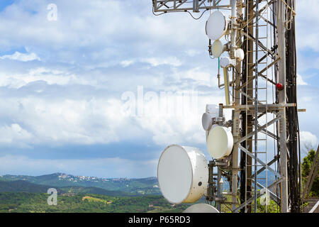 Torre di telecomunicazione con le antenne di comunicazione cellulari e sistemi radar. Contro il cielo nuvoloso sopra cime delle montagne verdi. Altezza di mountai Foto Stock