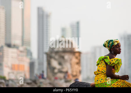 Una ragazza Afro-Colombian, vestito con il tradizionale 'palenquera' costume, attende per i turisti seduti sui muri di pietra a Cartagena, Colombia. Foto Stock