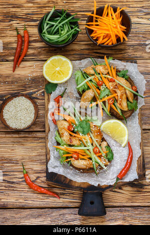 Asian sandwich con fritto di pollo e verdure fresche-carote, cetriolo, peperoncino, coriandolo e sesamo. Messa a fuoco selettiva. Vista superiore Foto Stock