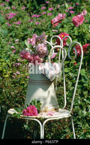 Still-Life della caraffa di rose rosa con cuore a forma di sacchetto di lavanda sul vecchio metallo bianco sedia da giardino Foto Stock