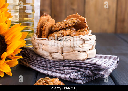 Dodsolnechnoe olio in una bottiglia grande, un bouquet di fiori di girasole, su un sfondo terned. In casa la cottura. Biscotti con semi. Prodotto naturale, in stile rustico. Spazio di copia Foto Stock