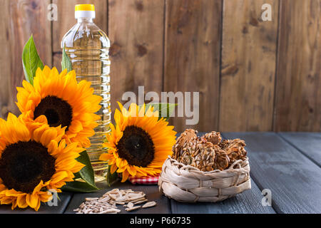 Dodsolnechnoe olio in una bottiglia grande, un bouquet di fiori di girasole, su un sfondo terned. In casa la cottura. Biscotti con semi. Prodotto naturale, in stile rustico. Spazio di copia Foto Stock